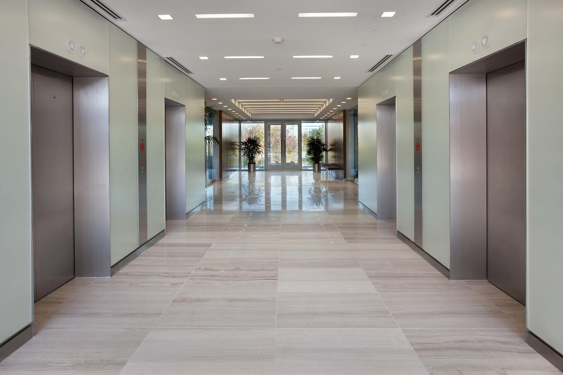 A hallway that is inside of an office building and there are elevators on either side of it to go up.