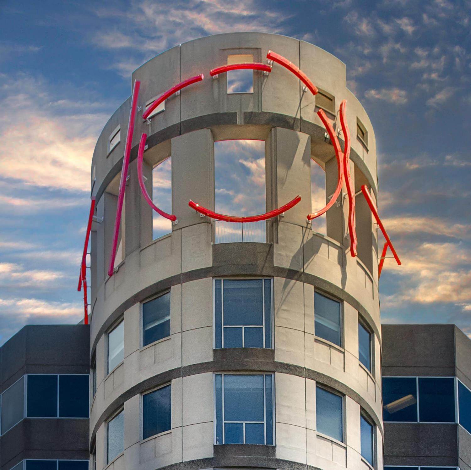A tower with the sky reflected in its windows and red scupture on the exterior.
