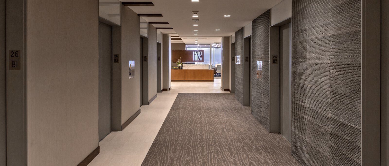 Hallway of elevators leading toward a receptionist desk.
