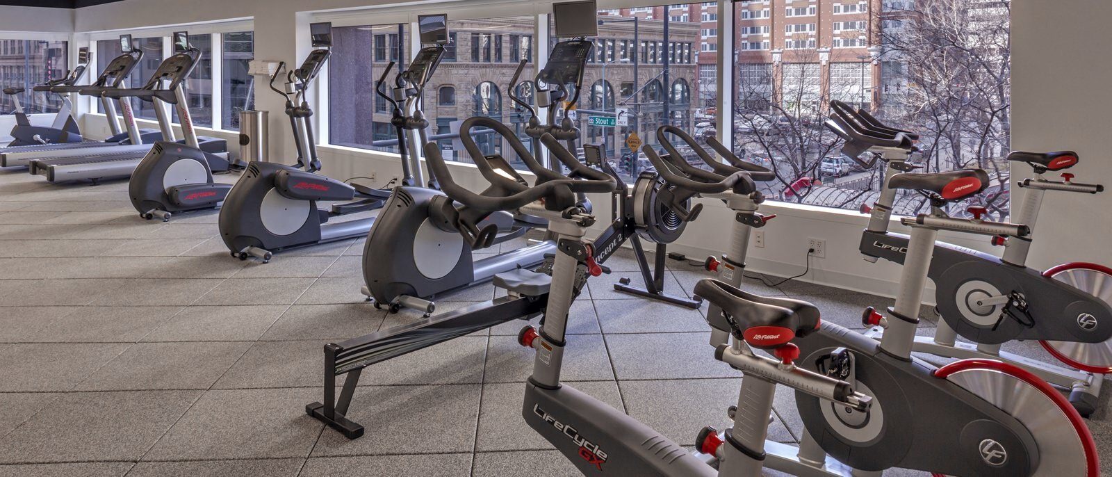 Inside of a gym with stationary bikes, ellipticals, and treadmills that look out onto a city street.