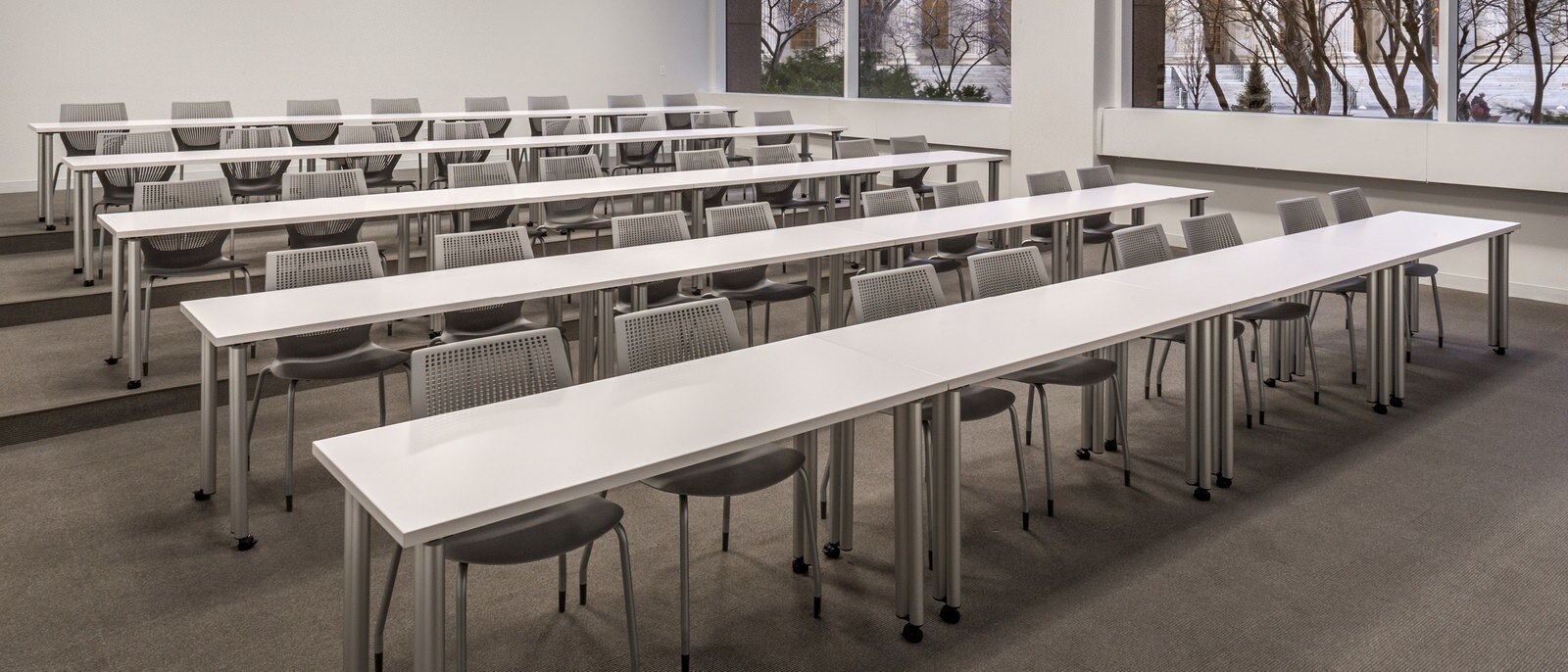 A classroom with five long white tables and multiple chairs.