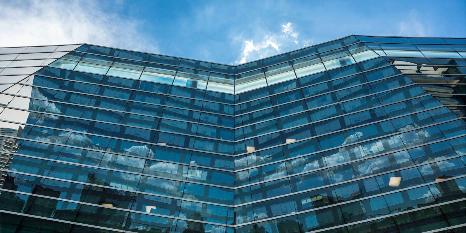 Upward view of a large building that is covered with glass windows with a blue sky above.