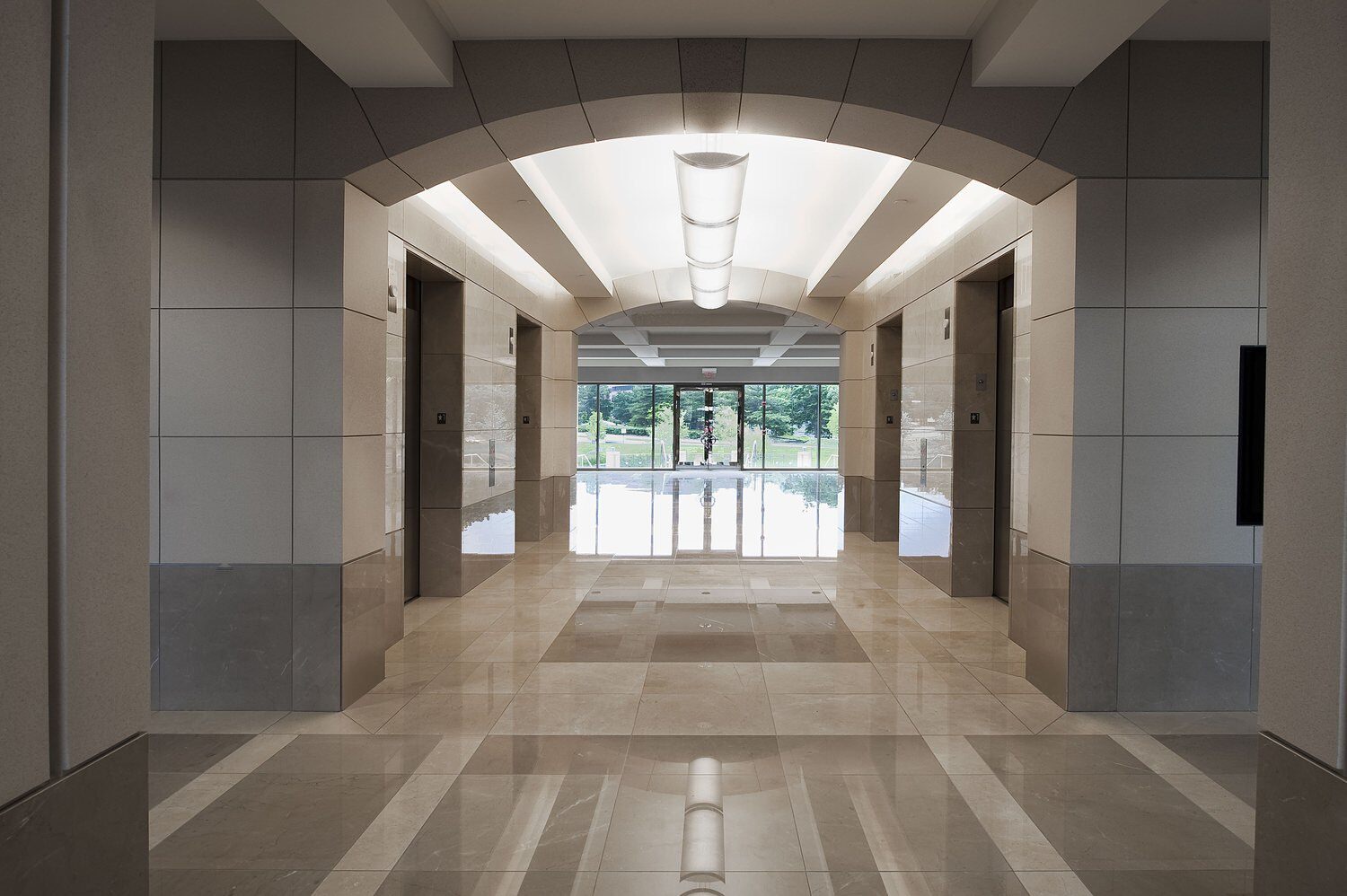 A corridor that leads through an office building and it has four elevator doors off of it.