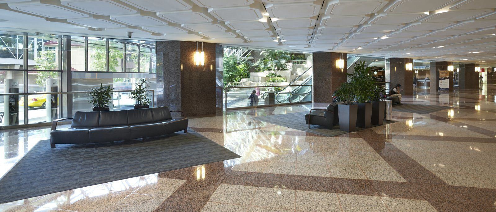 A lobby of a large building that has area rugs and couches scattered around it for people to sit.