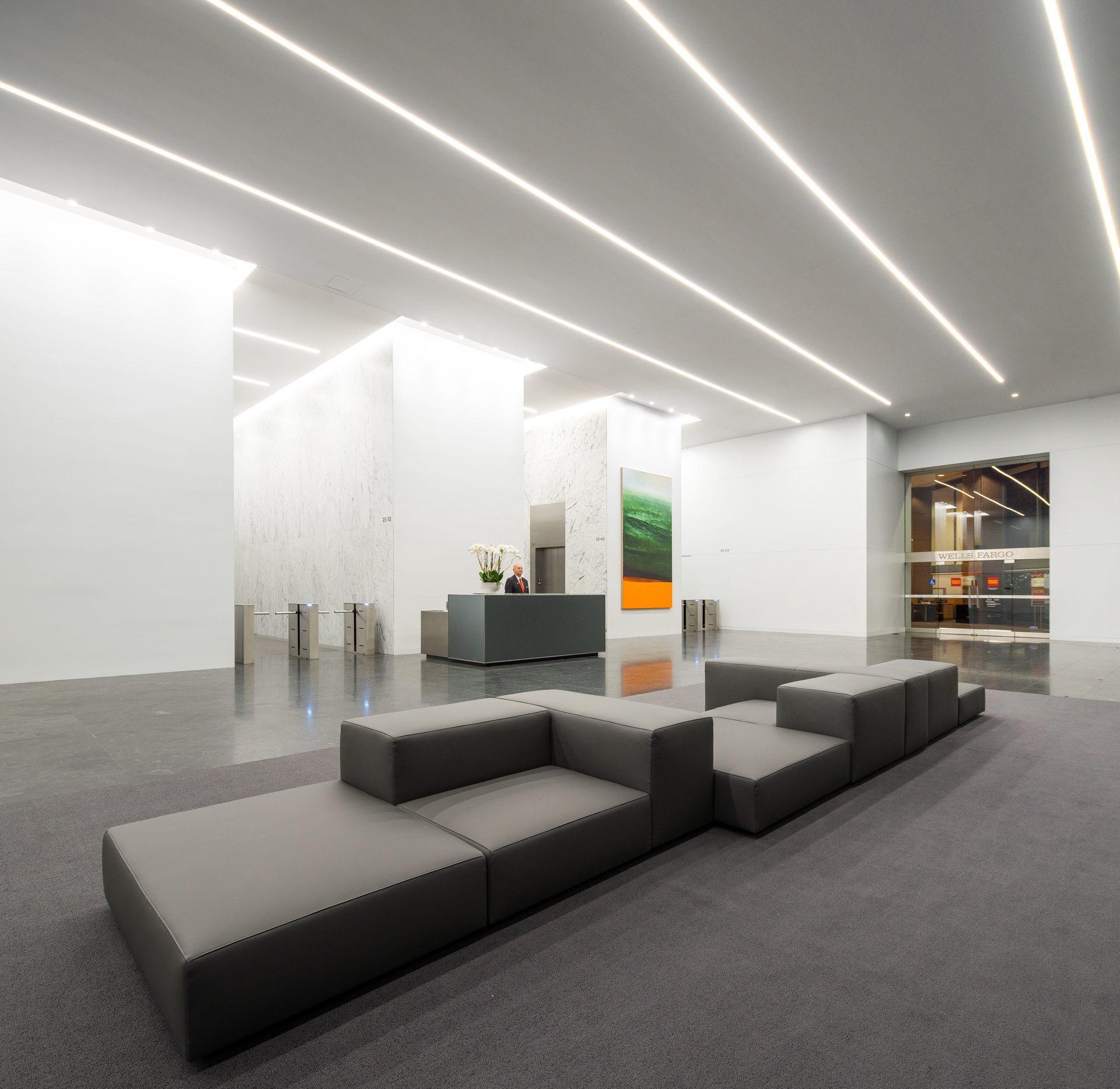 Bright lobby at night with gray couches and a turnstile.